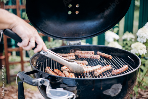 Backyard BBQ. Close-up of grilling sausages of meat on barbecue. Man preparing tasty sausages photo
