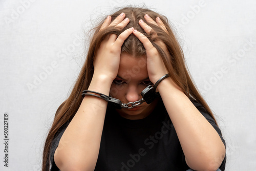 A young girl handcuffed on a gray background, close-up. Juvenile delinquent in a black T-shirt, criminal liability of minors. photo