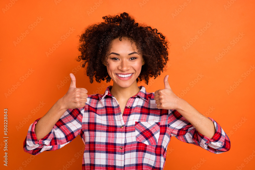 Photo of cute young brunette lady thumb up wear plaid shirt isolated on orange color background Photo of cute young brunette lady thumb up wear plaid shirt isolated on orange color background