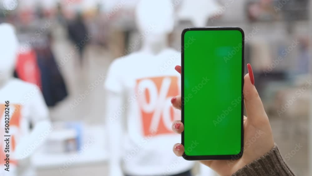 Big sale. Lots of discount coupons to save money on your smartphone. A girl is holding a phone with a green screen in a shopping center. black Friday. Big sale. Lots of discount coupons to save money on your smartphone. A girl is holding a phone with a green screen in a shopping center. black Friday.