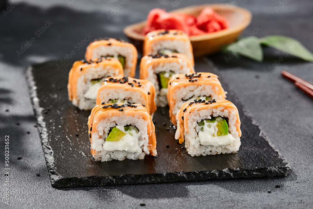 Maki sushi on dark slate. Hot philadelphia maki with baked salmon. Sushi roll with grilled salmon, cream cheese and avocado. Style concept japanese menu with black background, leaves and hard shadow. Maki sushi on dark slate. Hot philadelphia maki with baked salmon. Sushi roll with grilled salmon, cream cheese and avocado. Style concept japanese menu with black background, leaves and hard shadow.
