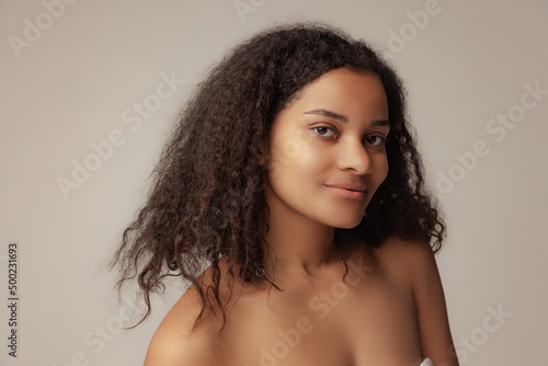Close-up portrait of young beautiful woman with curly hair posing isolated over grey background. Natural beauty concept
