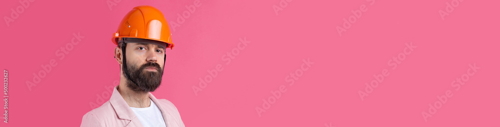 Portrait of young construction engineer wear orange hard hat, in a pink jacket standing on red studio background. Portrait of young construction engineer wear orange hard hat, in a pink jacket standing on red studio background.
