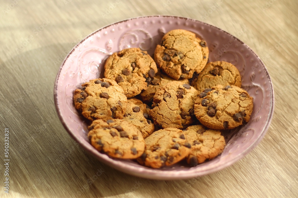 Pink plate filled with chocolate chip cookies on wooden table. Selective focus. Pink plate filled with chocolate chip cookies on wooden table. Selective focus.