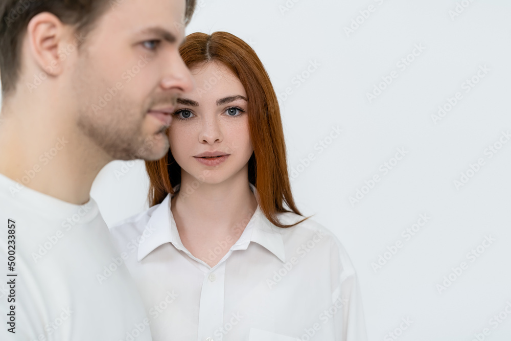 Young woman looking at camera near blurred boyfriend isolated on white.