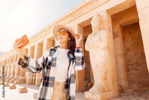 Travel blogger girl takes selfie pictures on a smartphone at the famous Hatshepsut temple in the ancient city of Luxor in Egypt. Tourism attractions and destinations