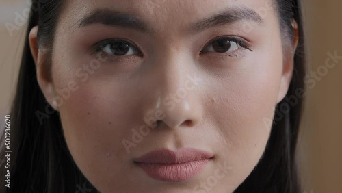 Extreme close up Asian woman face portrait body part perfect clean young skin after beauty treatment natural makeup wide eyebrows friendly expression Korean woman lady looking at camera good eyesight photo
