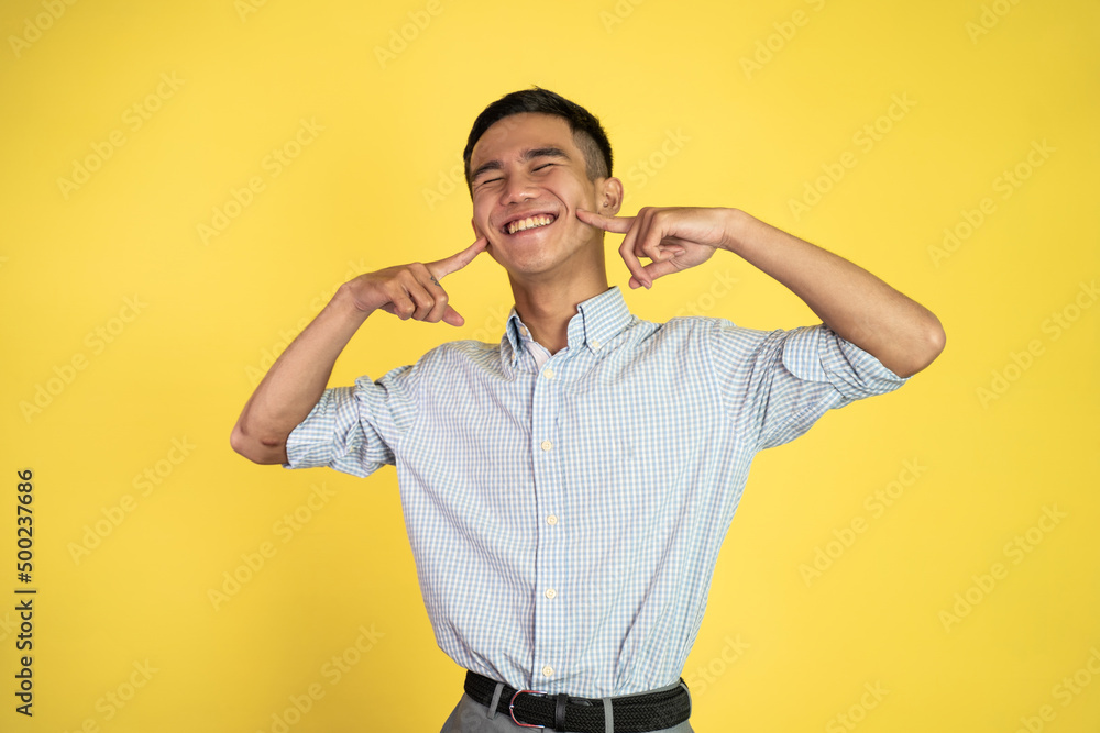 asian young man smiling and making a cute gesture put his finger in the cheeks asian young man smiling and making a cute gesture put his finger in the cheeks