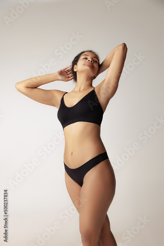 Portrait of young woman with natural body posing in black underwear isolated over grey studio background © master1305