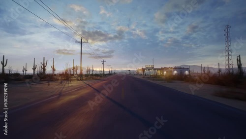 A drone flies straight over a long and empty road in the middle of the desert next Gasstation