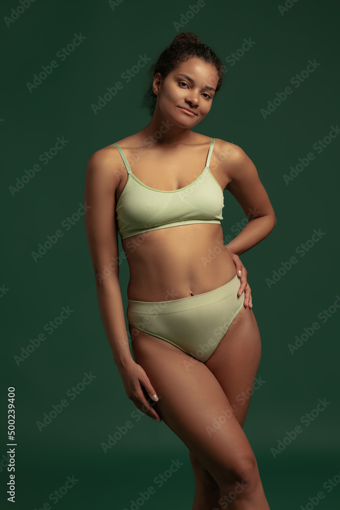 Portrait of young woman posing in underwear isolated over green studio background. Natural body Portrait of young woman posing in underwear isolated over green studio background. Natural body