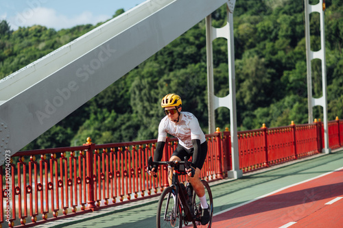 A male professional cyclist rides a bicycle across the bridge and looks to the side. Training on a bicycle.