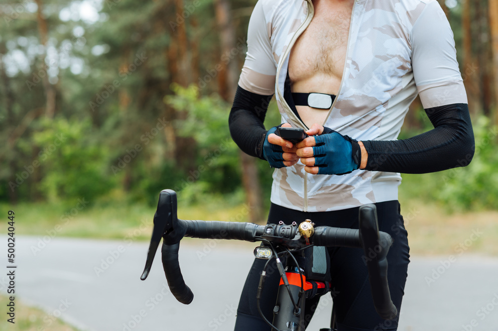 Obraz premium Male cyclist athlete with a heart rate monitor on his body uses a bicycle computer while training in the woods outside the city.
