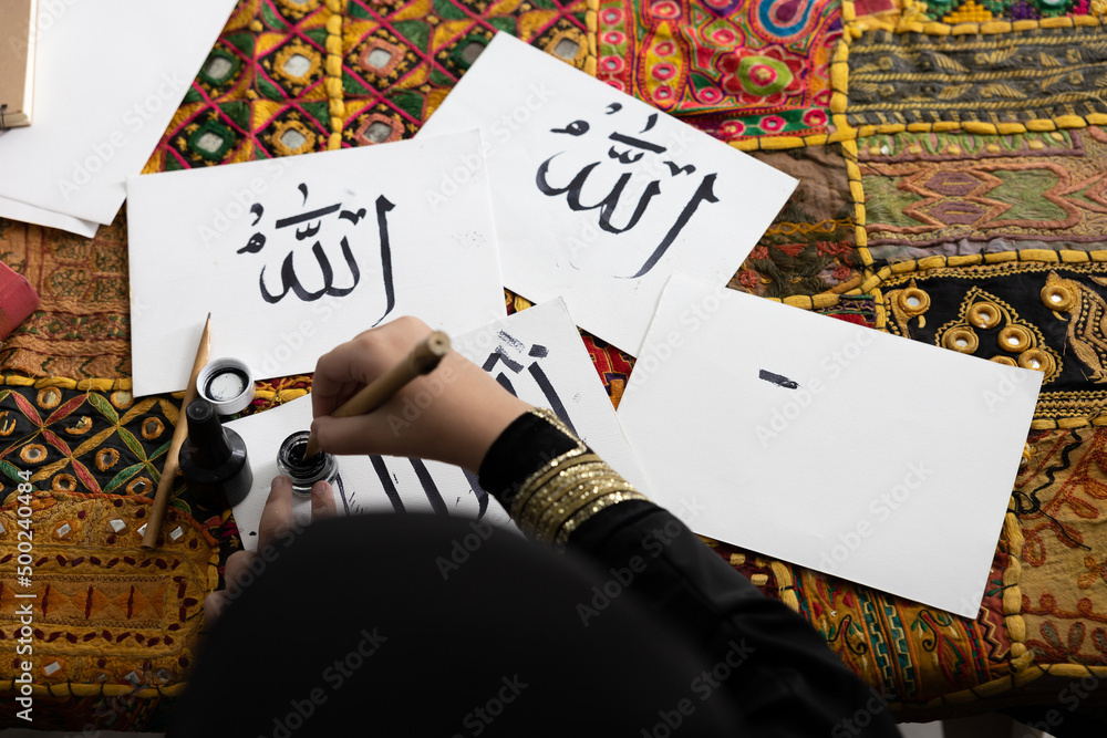 close up muslim girl hands writing Arabic text with bamboo pens and