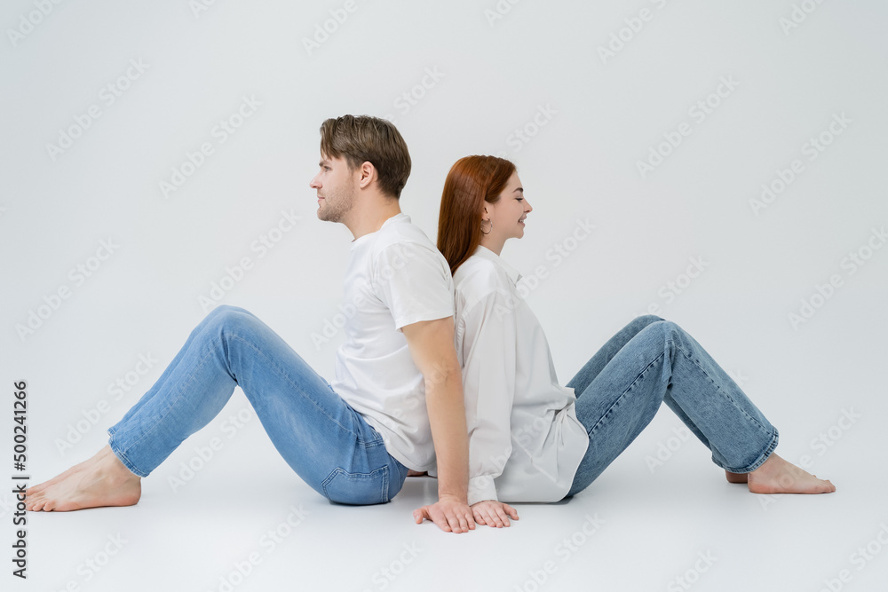 Side view of young couple sitting back to back on white background. Side view of young couple sitting back to back on white background.