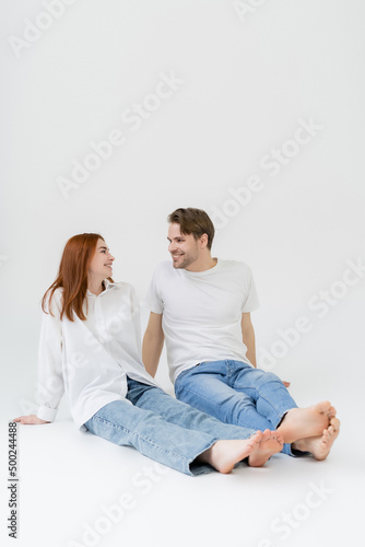 Positive barefoot couple looking at each other on white background.