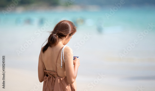 The shoulder of Asian Thai Woman from backside who play mobile at outdoor field sea beach blur background. photo