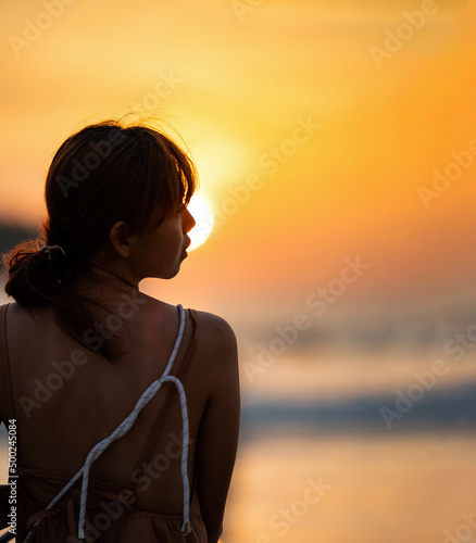 Asian Woman in Silhouette mood and tone of picture with orange warm sunset blurs, background on Kata Beach, Phuket province, Thailand. © Surachetsh