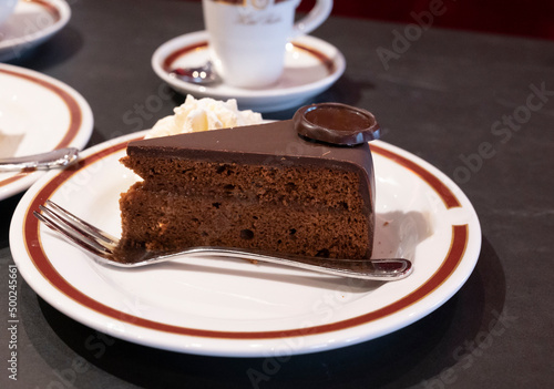 Piece of famous Sachertorte chocolate cake with apricot jam of Austrian origin served with whipped cream and black coffee photo
