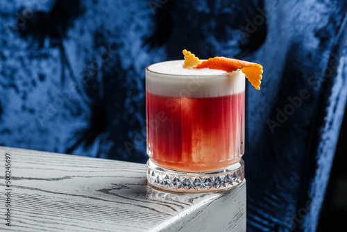 Classic old fashioned red Cocktail in a retro glass with ice and orange peel on a blue background, top view