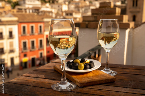 Two glasses of Spanish dry rueda white wine served with olives on roof terrace with view on old part of Andalusian town Granada, Spain