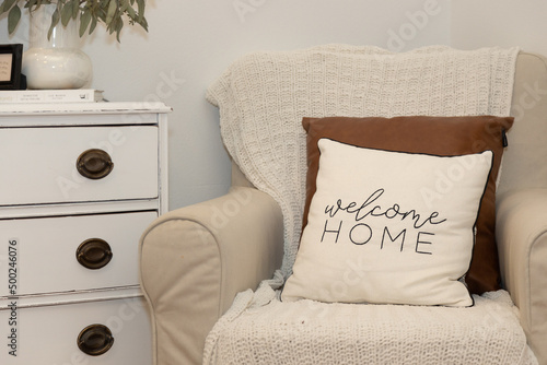 Welcome home pillow on beige chair in bedroom