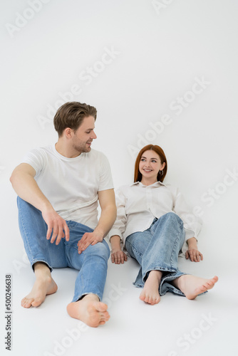 Positive barefoot couple sitting on white background.