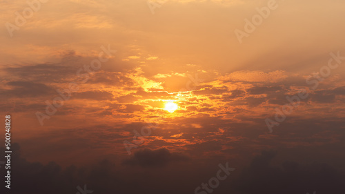 the brightest sun is shining from behind the clouds on the morning orange sky © c_atta