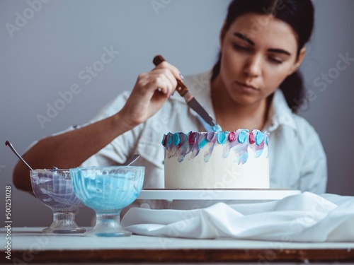 Billede på lærred Young girl confectioner decorates homemade cake with a special spatula
