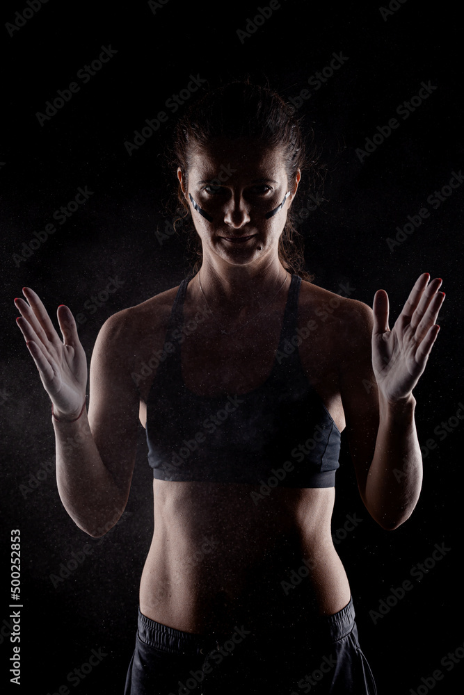 Obraz premium Kickboxer kirl with magnesium powder on her hands punching with dust visible..