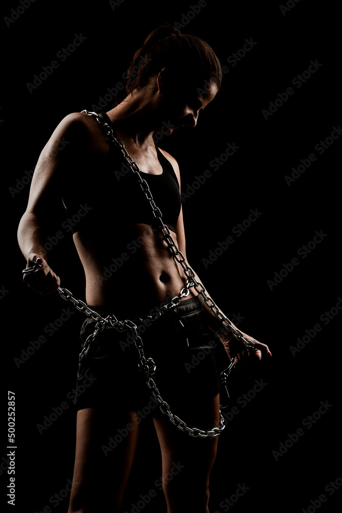 Strong fit girl with metal chain. Pulling and posing against black background..