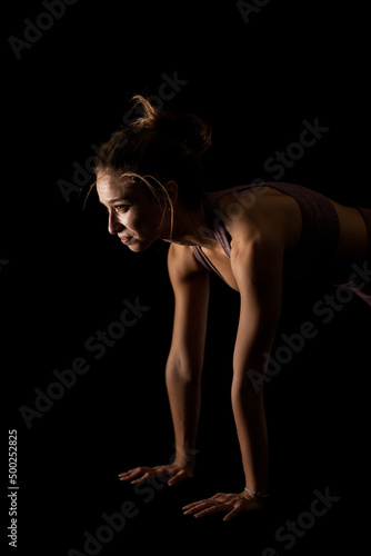 Fit woman practicing yoga poses. Side lit half silhouette girl doing exercise in studio against black background.. © Nikola Spasenoski