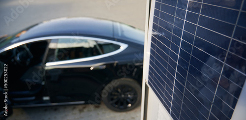 Fototapeta Naklejka Na Ścianę i Meble -  On the blurred backdrop of black elite car close up view of one solar panel. Concept ecological electric vehicle as alternative to fuel-powered transport.