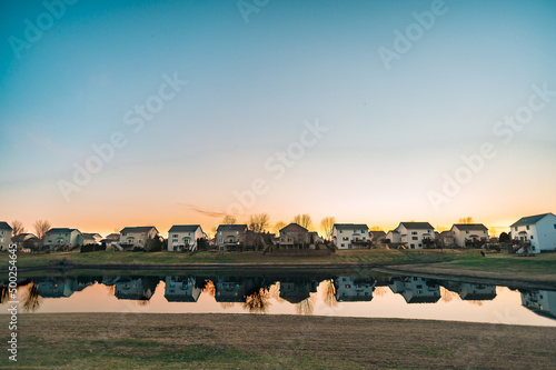 A row of suburban houses overlook a small pond during sunset with room for copy