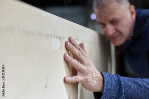 Mature carpenter checks the quality of the plywood frame. Inspection and quality control of the work performed or the quality of wood. The master receptionist at the furniture production.