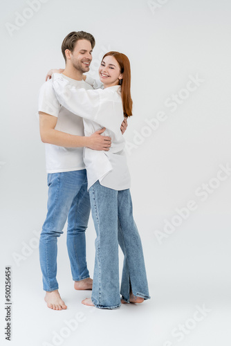 Full length of young barefoot woman embracing boyfriend on white background.