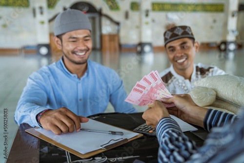 portrait of male muslim paying some zakat charity using cash at the mosque. indonesian money rupiah bank note for zakat