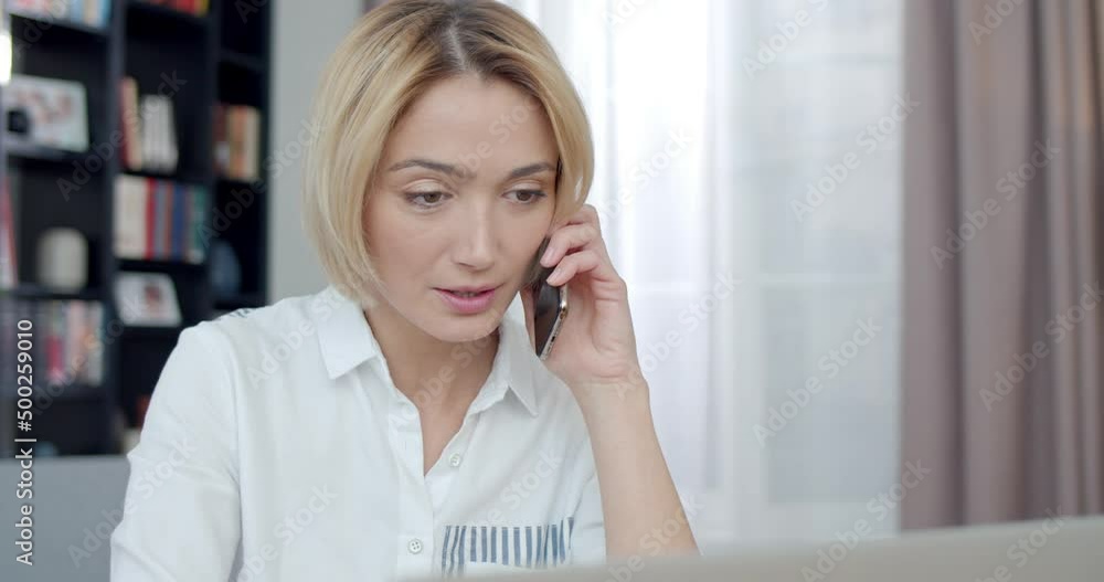 Caucasian business lady in stylish white shirt working on wireless laptop while having mobile conversation at home. Modern gadgets, lifestyles and people concept. Caucasian business lady in stylish white shirt working on wireless laptop while having mobile conversation at home. Modern gadgets, lifestyles and people concept.