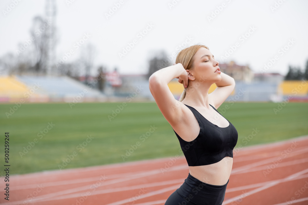 sportswoman with closed eyes and hands behind head warming up on stadium. sportswoman with closed eyes and hands behind head warming up on stadium.