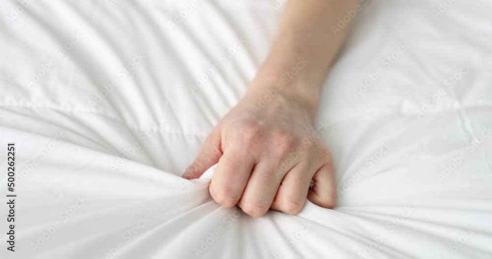 Woman hand clutches blanket on bed in pain Woman hand clutches blanket on bed in pain