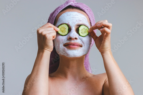 Beautiful young woman applying facial cosmetics skincare mask and slices of cucumber.