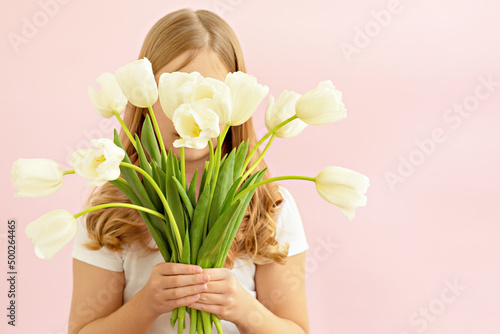 The concept of spring, happiness and holiday. Close-up portrait of a beautiful smiling girl holding a bouquet of white tulips in her hands eyes closed on a pink background