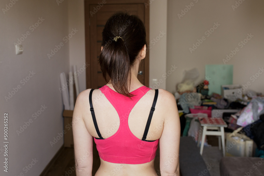 beautiful sports girl at home. the girl is preparing to start cleaning. girl's back. pink sports t-shirt and hair gathered in a ponytail.