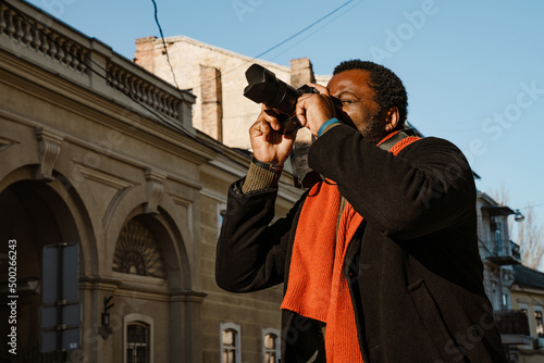 Black mid man taking photo while walking at city street photo