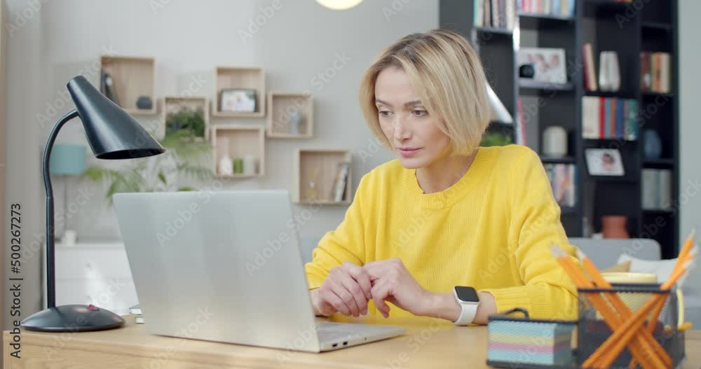 Upset caucasian woman in yellow sweater sitting at desk and reading bad news in modern laptop. Life problems, people and negative feelings concept. Upset caucasian woman in yellow sweater sitting at desk and reading bad news in modern laptop. Life problems, people and negative feelings concept.