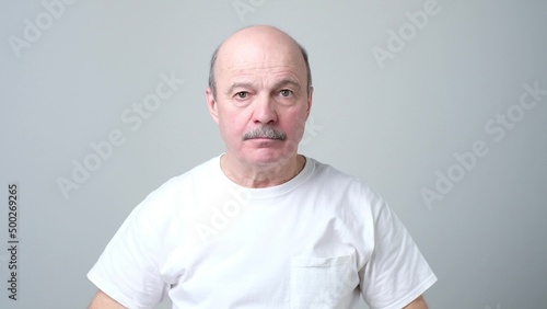 Senior hispanic man with mustache looking at camera without emotions.