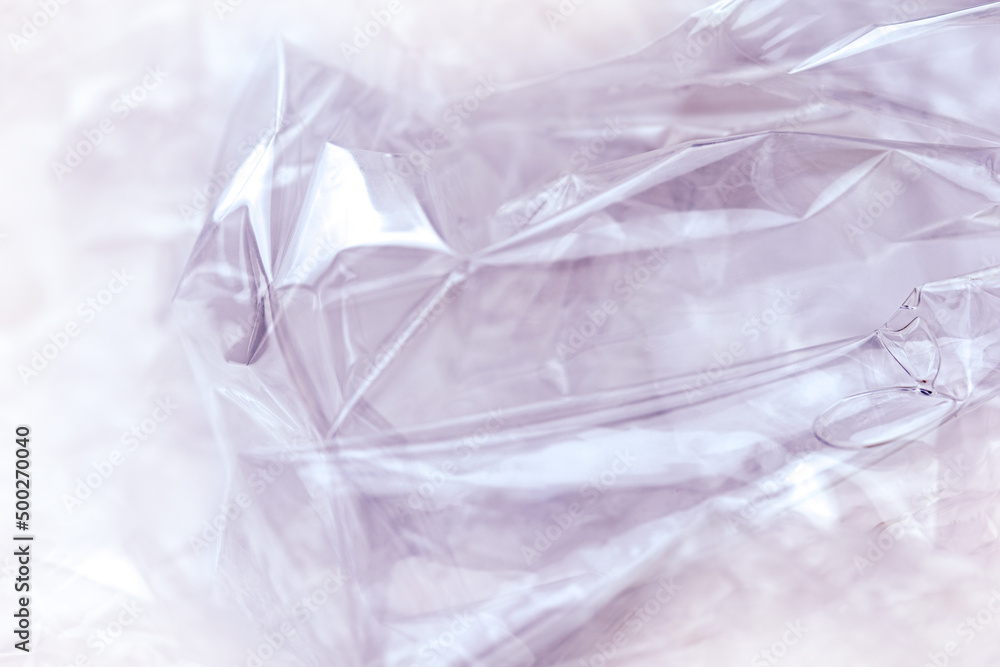 Texture of a plastic transparent cellophane package on a purple background. The plastic surface is wrinkled and torn, forming an abstract pattern. Texture of a plastic transparent cellophane package on a purple background. The plastic surface is wrinkled and torn, forming an abstract pattern.