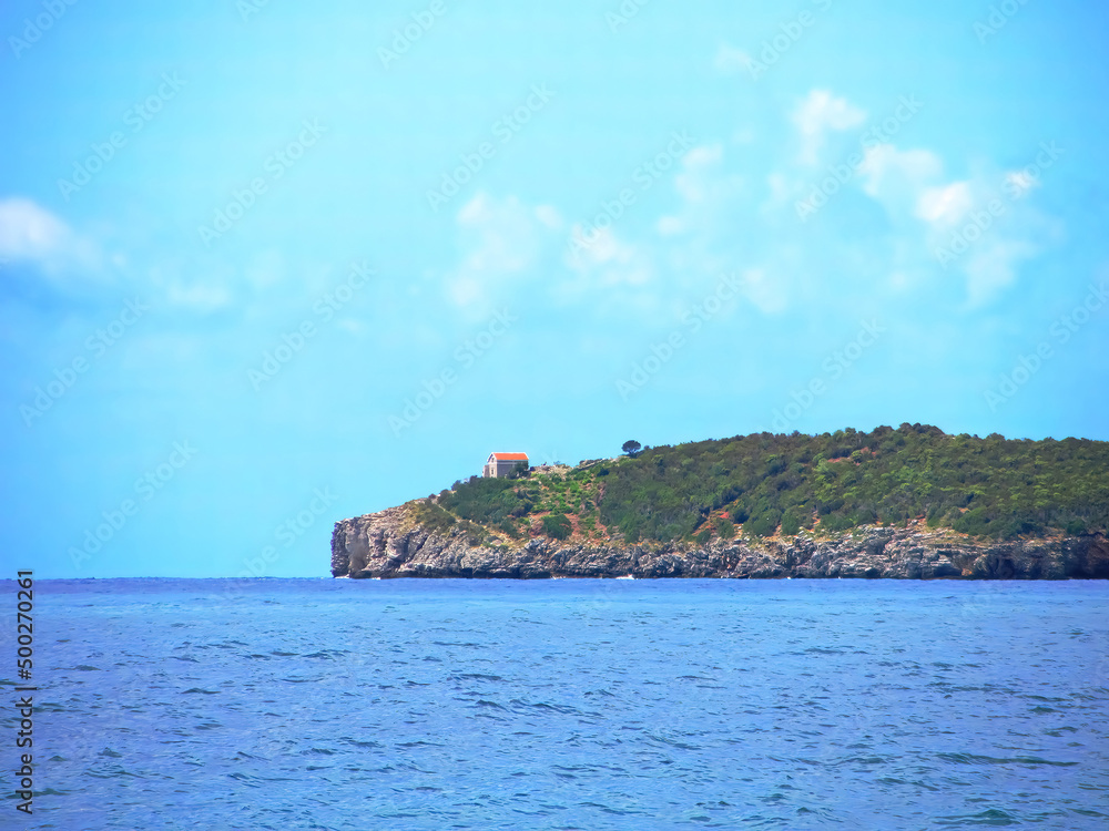 A lonely house with a colored roof stands on a green island in the middle of the sea. The steep slopes on a cliff island on a bright summer day