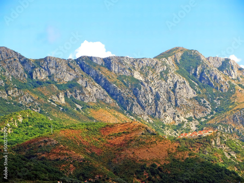 A wall of mountains rises above the valley. Warm tones on a sunny day with a small village in the hills. Mountains rock granite