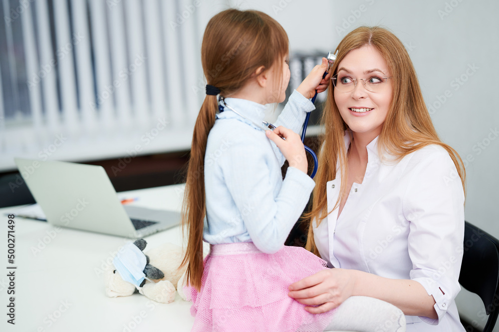 Obraz premium Little girl patient use stethoscope and play with female caucasian doctor in her office